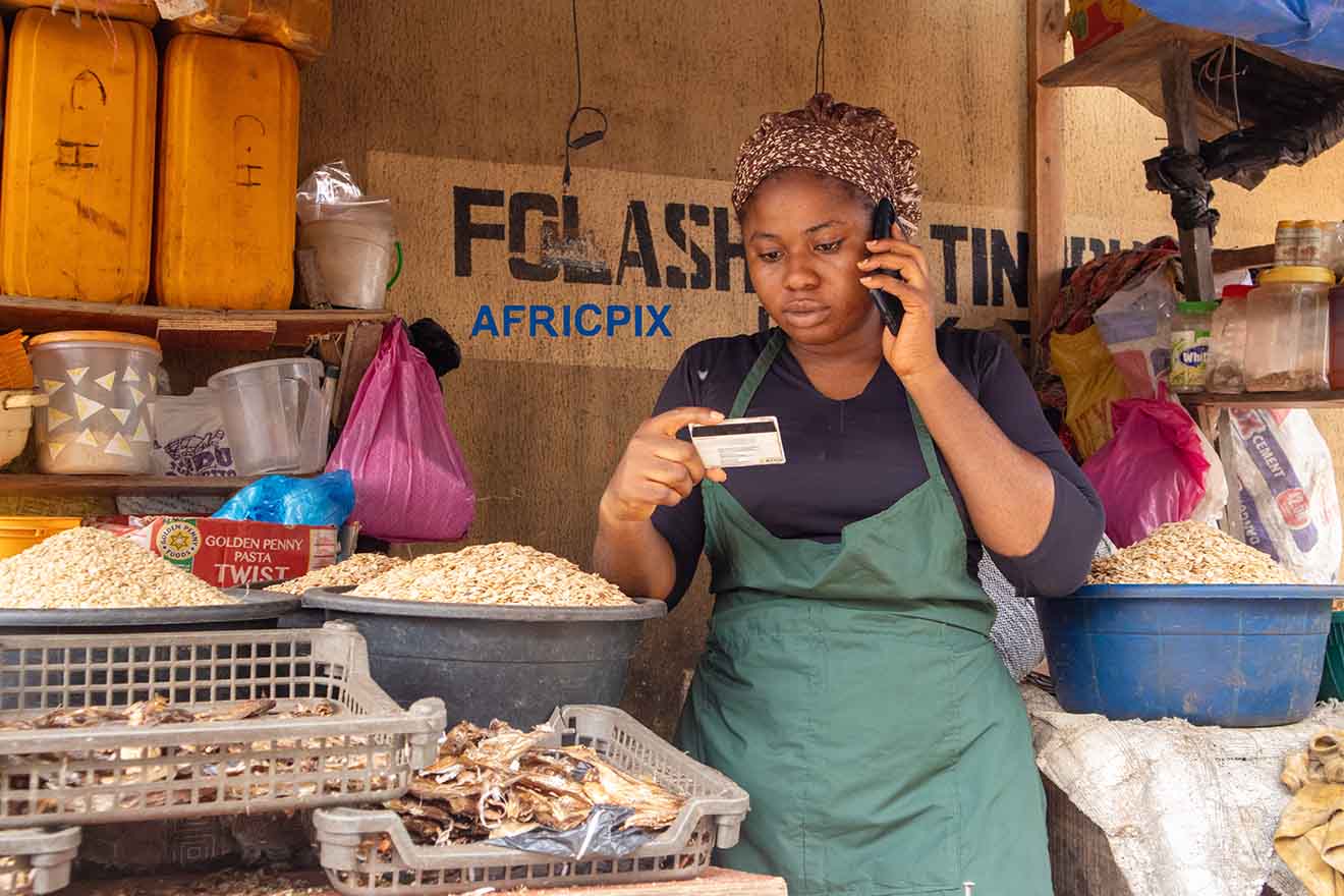 Happy Market Woman Making a Call While Referencing ATM Numbers